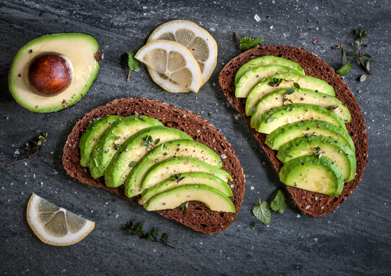 two slices of toast with avocado and lemon slices.