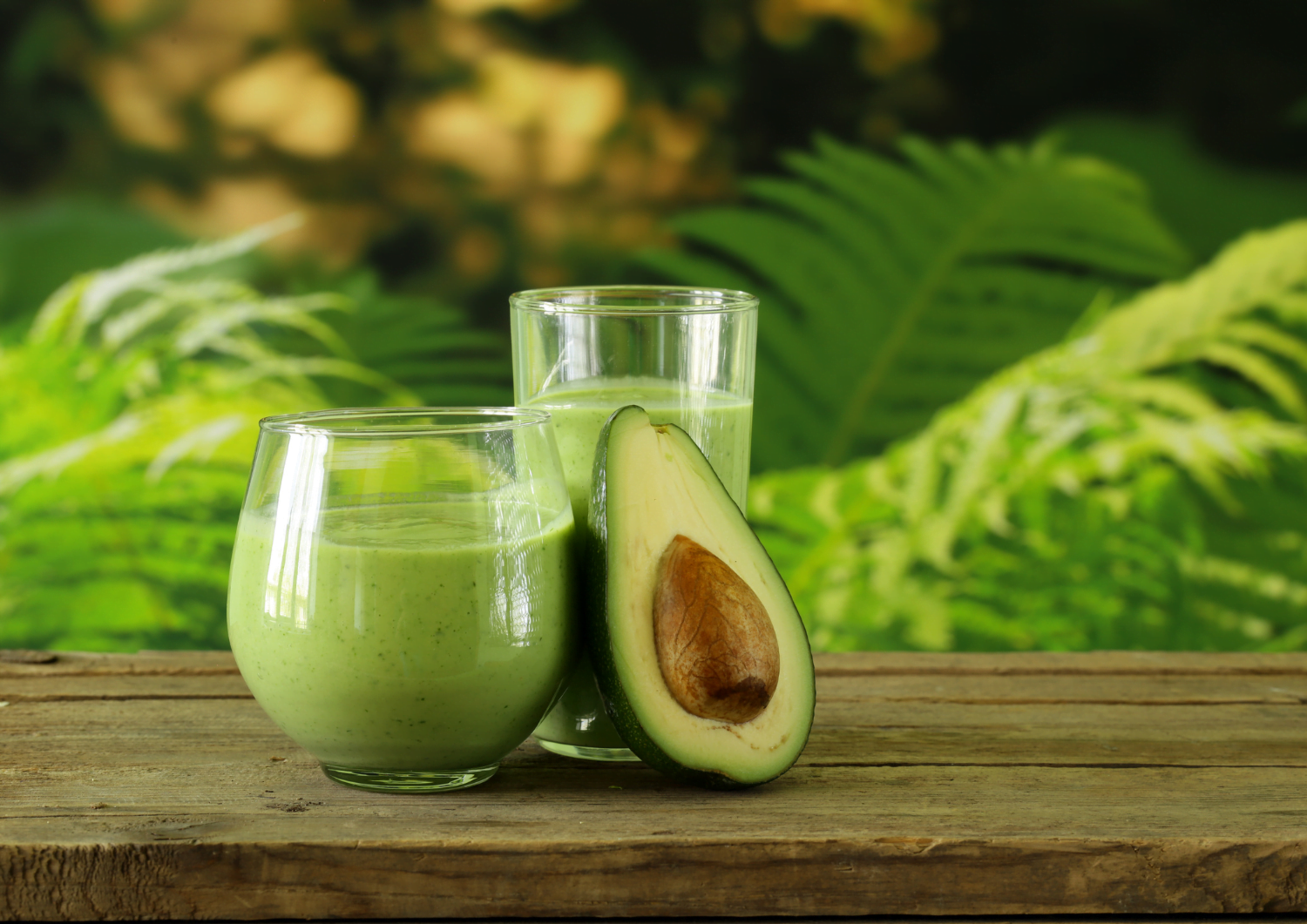 two glasses of green smoothie on a wooden table.